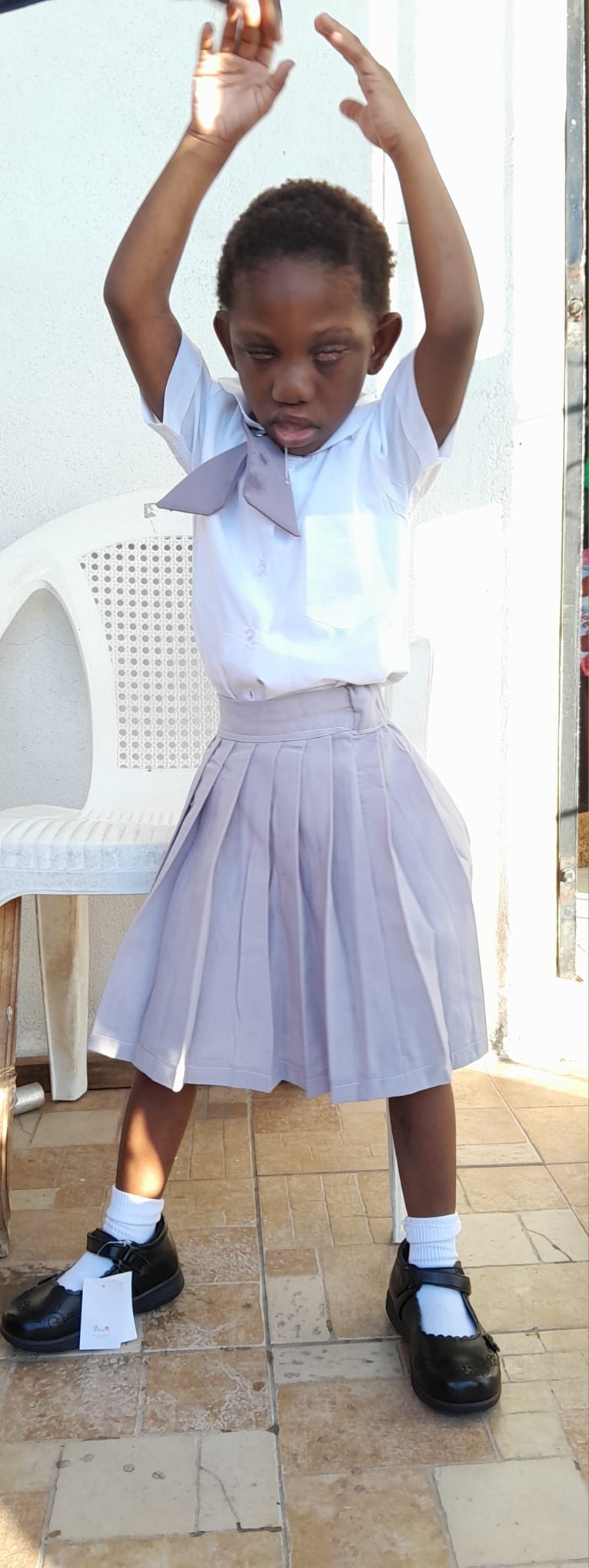 Ja’Dei Grant standing in a wide stance in her school uniform with both arms raised above her head, illuminated by bright sunlight.
