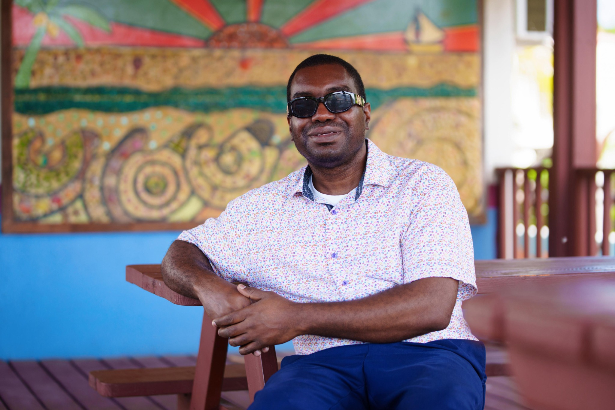 Kevin E. Cartwright seated at a wooden table with a colorful Bahamian-style mural in the background.